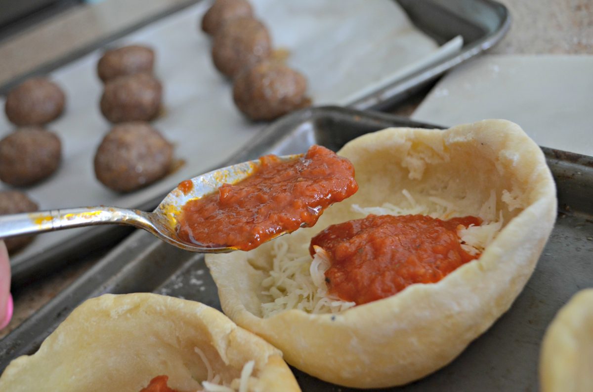 Adding sauce to meatball pizza bowls before baking