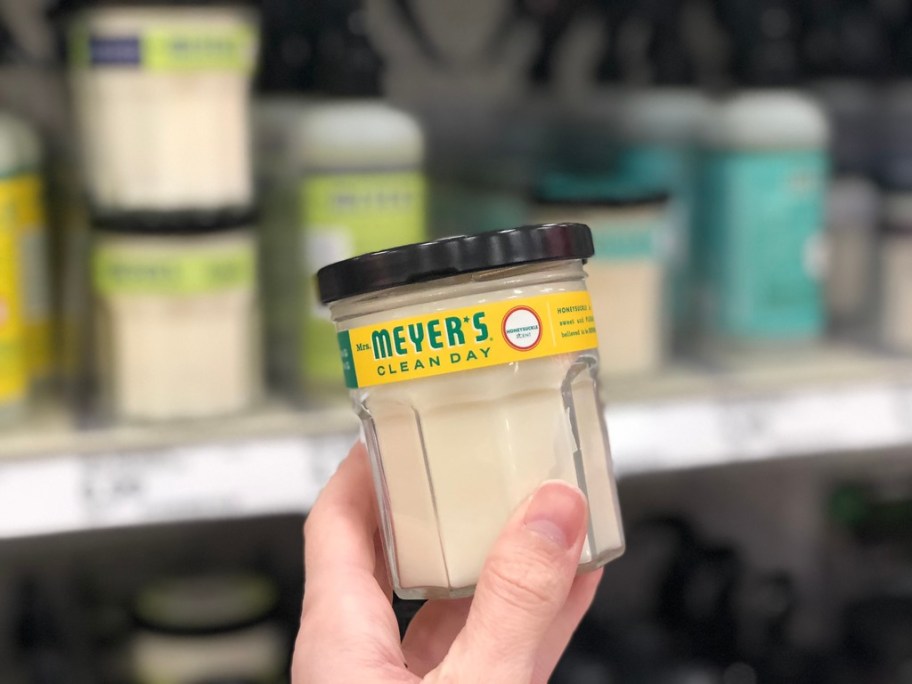 hand holding a glass jar candle in a store, more candles on the shelf behind it