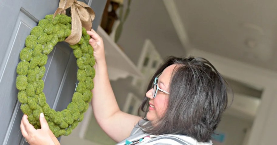 woman hanging moss wreath on front door