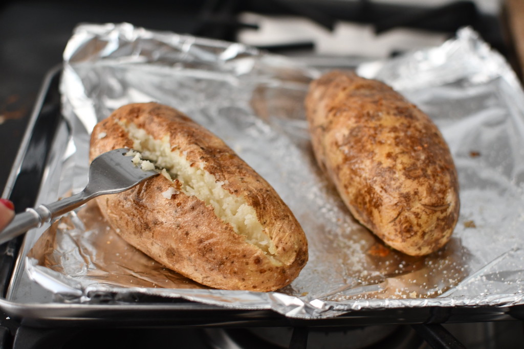 two large bakd potatoes on sheet pan with aluminum foil