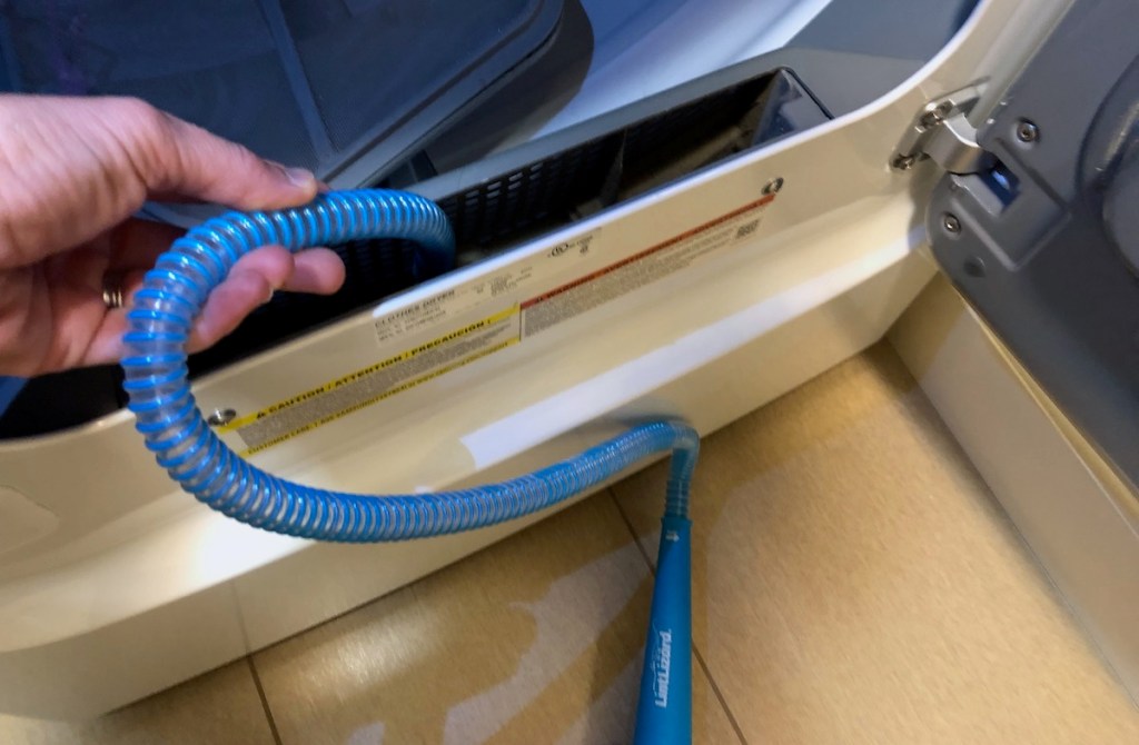 hand holding blue hose in dryer vent opening