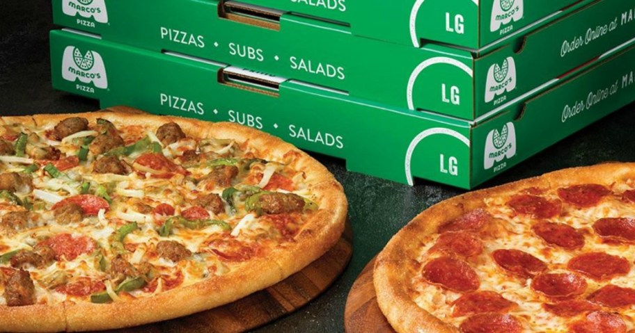two pizzas in front of a stack of pizza boxes
