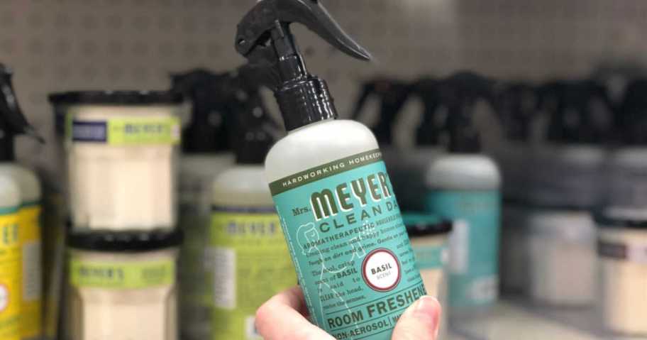 hand holding bottle of Mrs. Meyer's Room Freshener Basil 8 oz with other mrs. meyers
