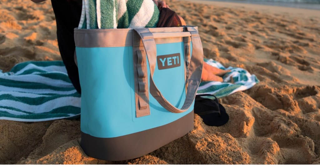 person sitting in the sand next to a blue yeti carryall