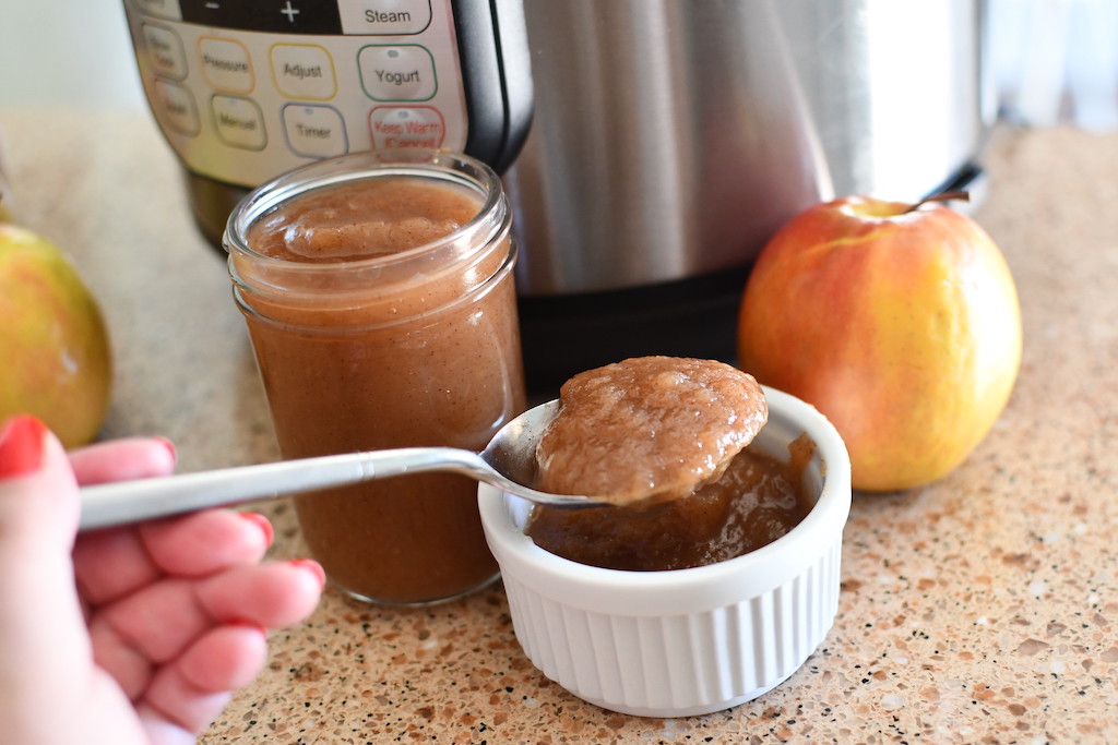 homemade applesauce on spoon with Instant Pot and apples in the background
