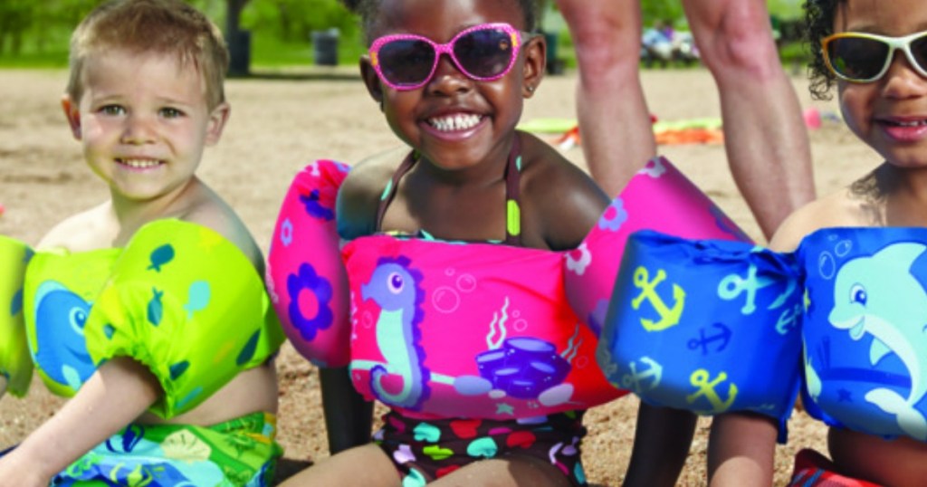 three kids sitting on beach with smiles and sunglasse