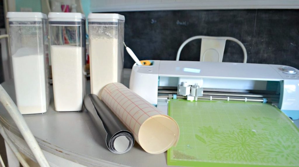 containers with dry baking food and rolls of adhesive sticker sitting next to cricut maching