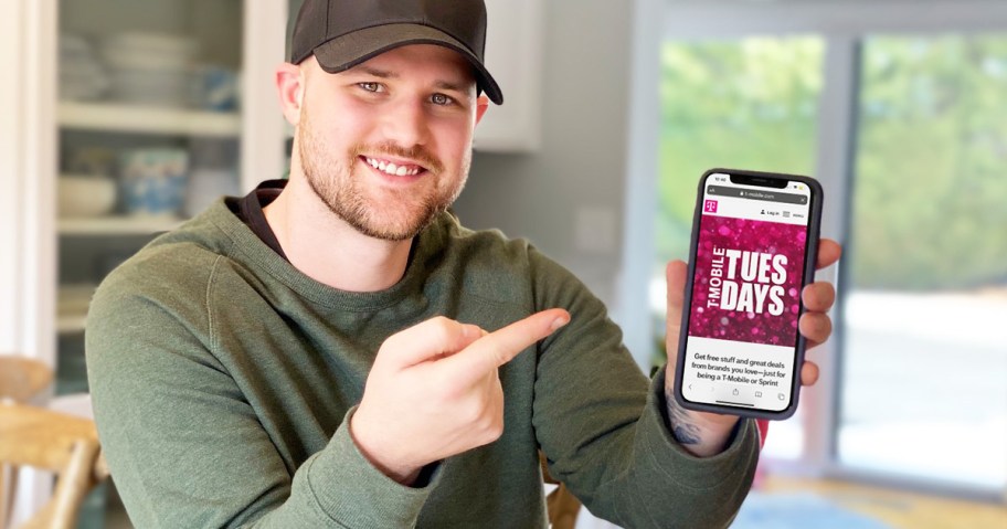 man in olive green hoodie pointing at an iphone with t-mobile tuesdays app