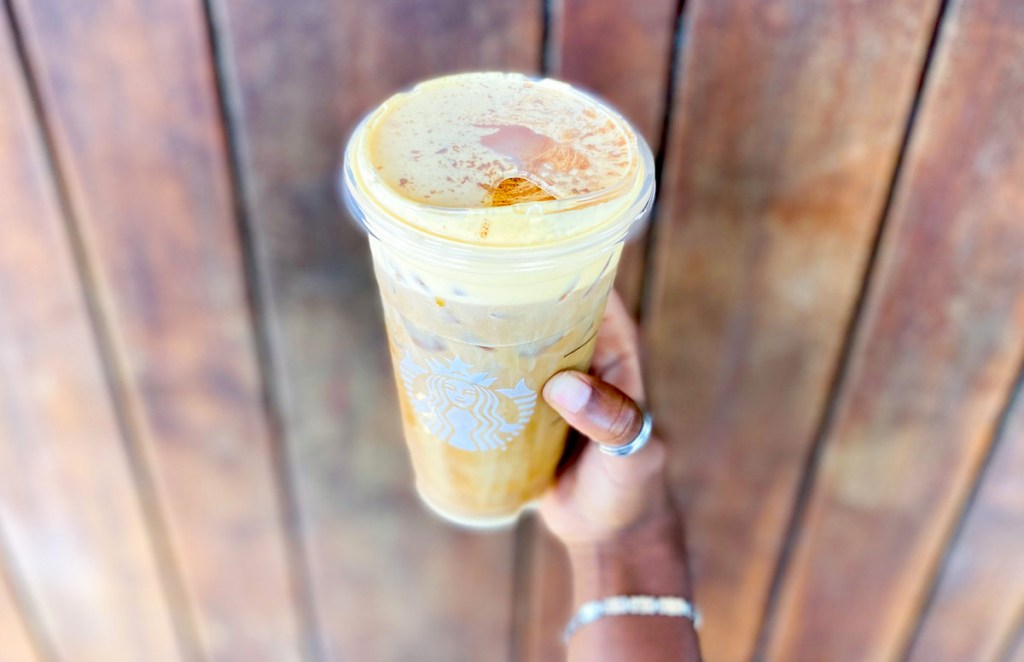hand holding starbucks coffee drink in front of wood wall