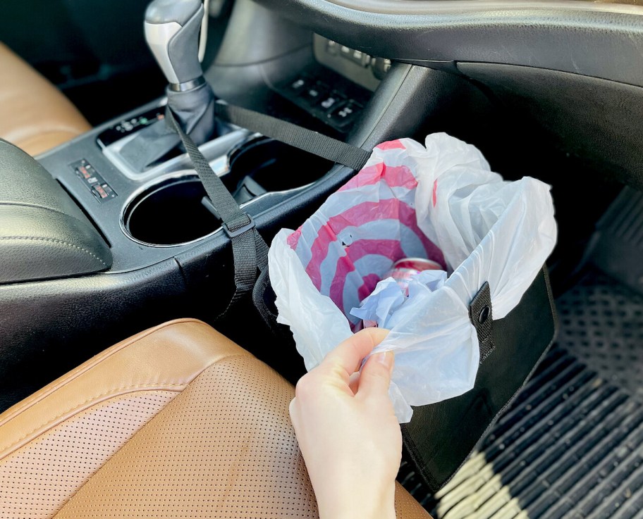 hand holding edge of mini trash can, one of our car organizer ideas, hanging over car floor