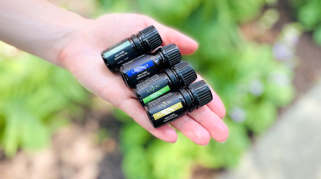 hand holding four mini bottles of anjou essential oils outside
