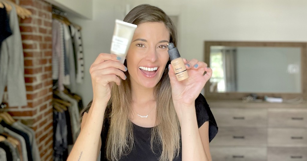 woman holding up two beauty products in bedroom
