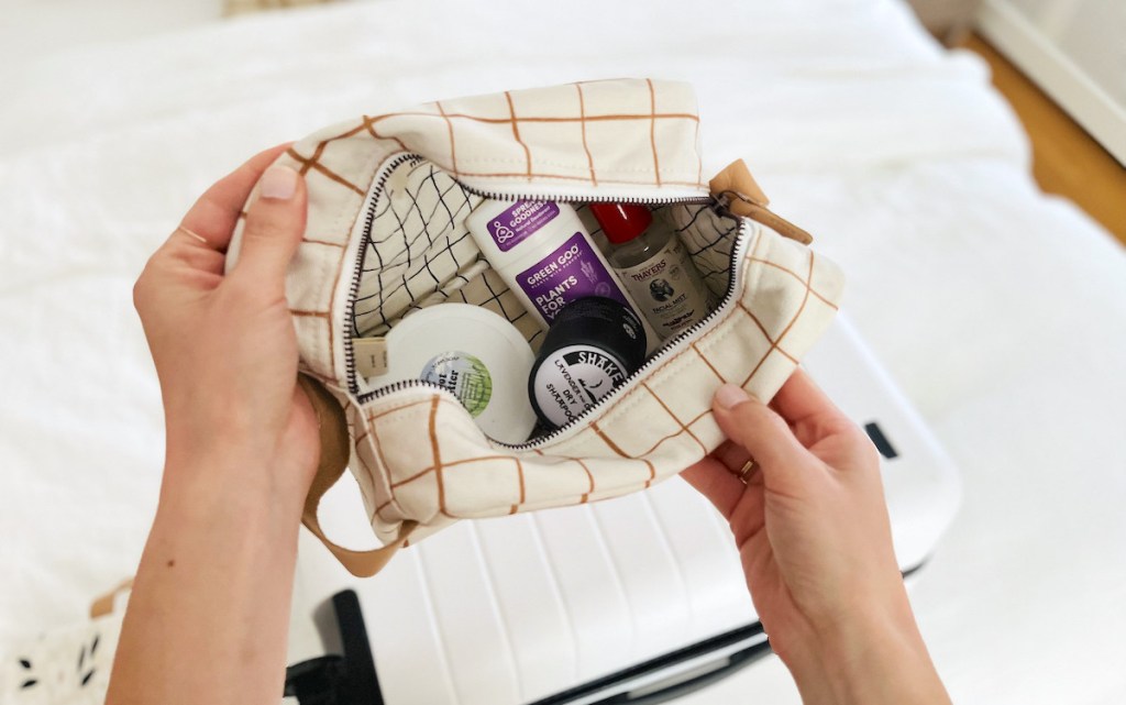 hand holding open white and brown bag with beauty essentials inside