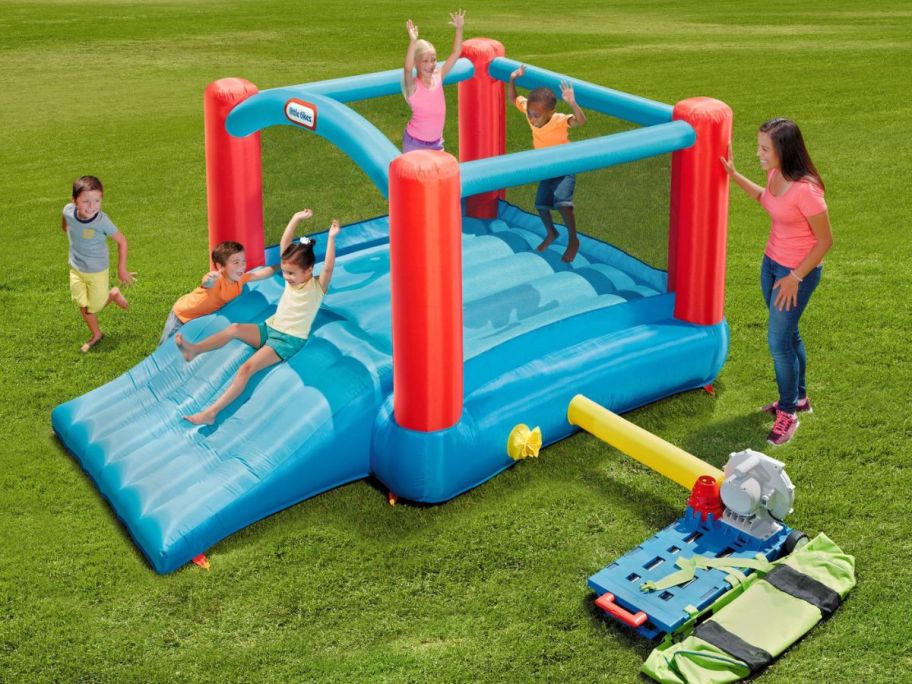 kids playing on little tikes bounce houdse outside with adult standing next to it