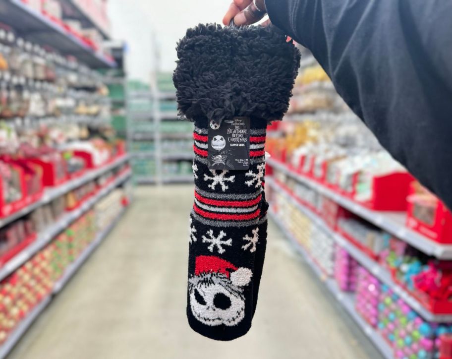 a womans hand holding a pair of jack skellington slipper socks