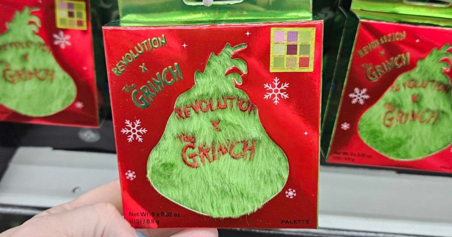 hand holding a red makeup pallet with The Grinch on the cover 