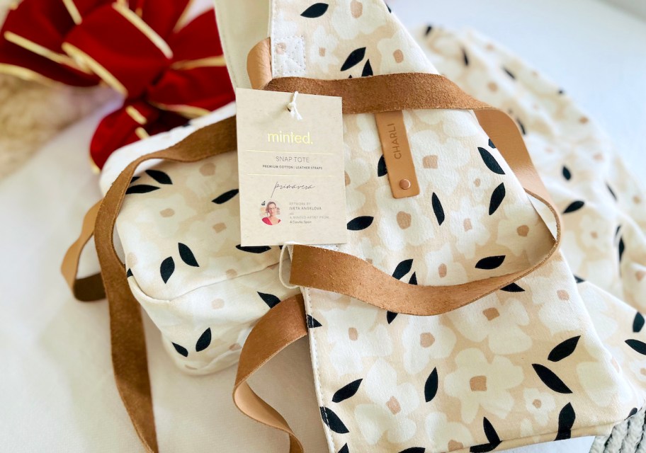 minted snap tote with tag laying on white couch with red bow