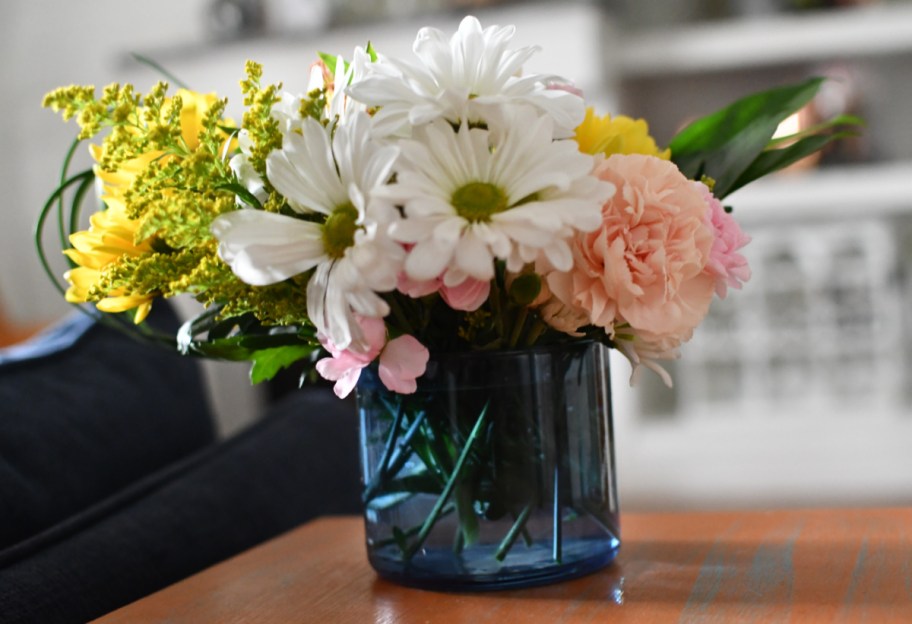 A candle jar vase with daisies and carnations
