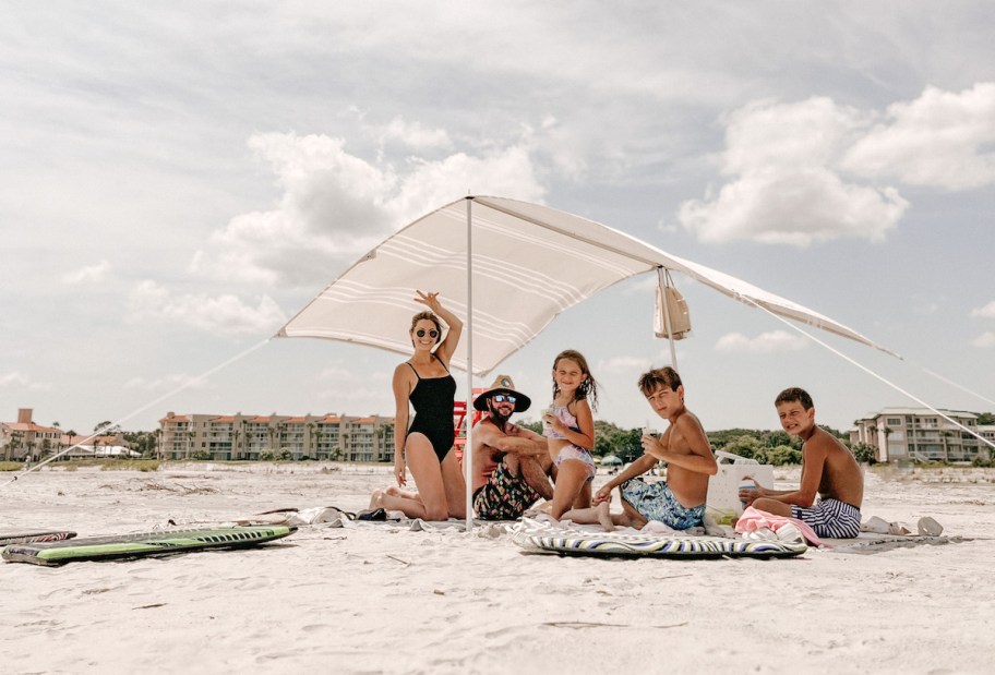 family sitting under beach umbrella 