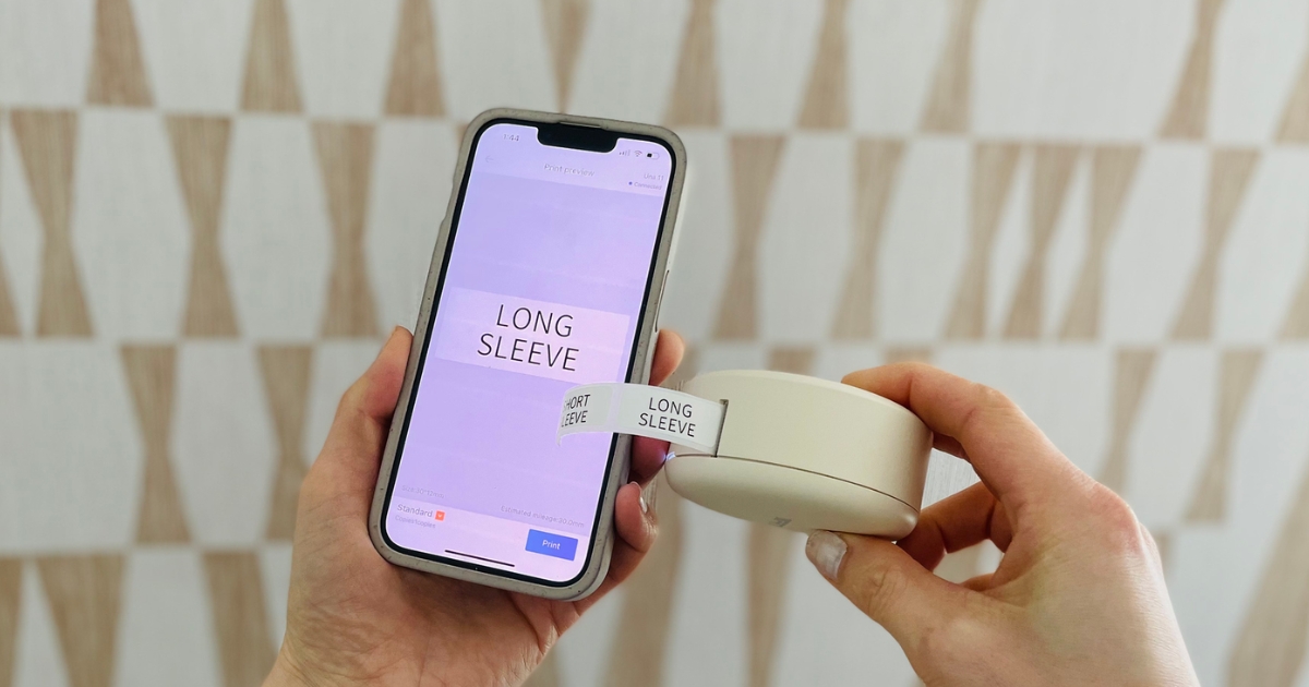 hand holding an iDPRT Bluetooth Thermal Label Maker in Beige next to a smartphone