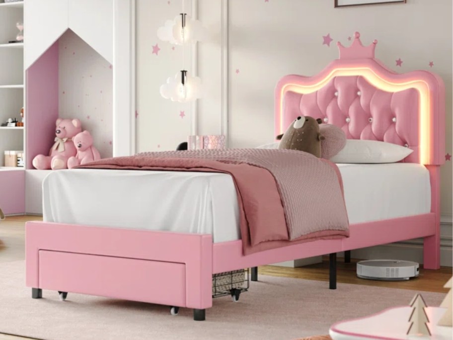 light pink twin bed with crown shaped headboard with lights around it and pink bedding in a kids room