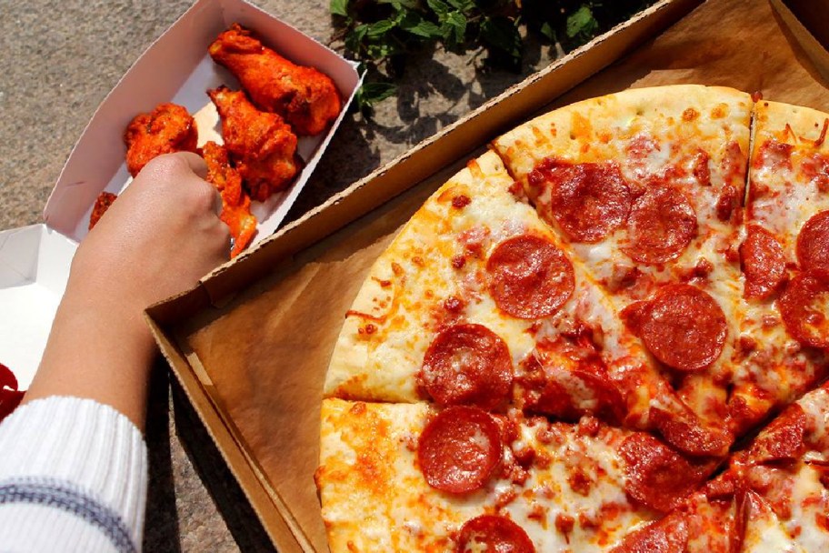 woman grabbing a chicken wing next to a 7-eleven pizza