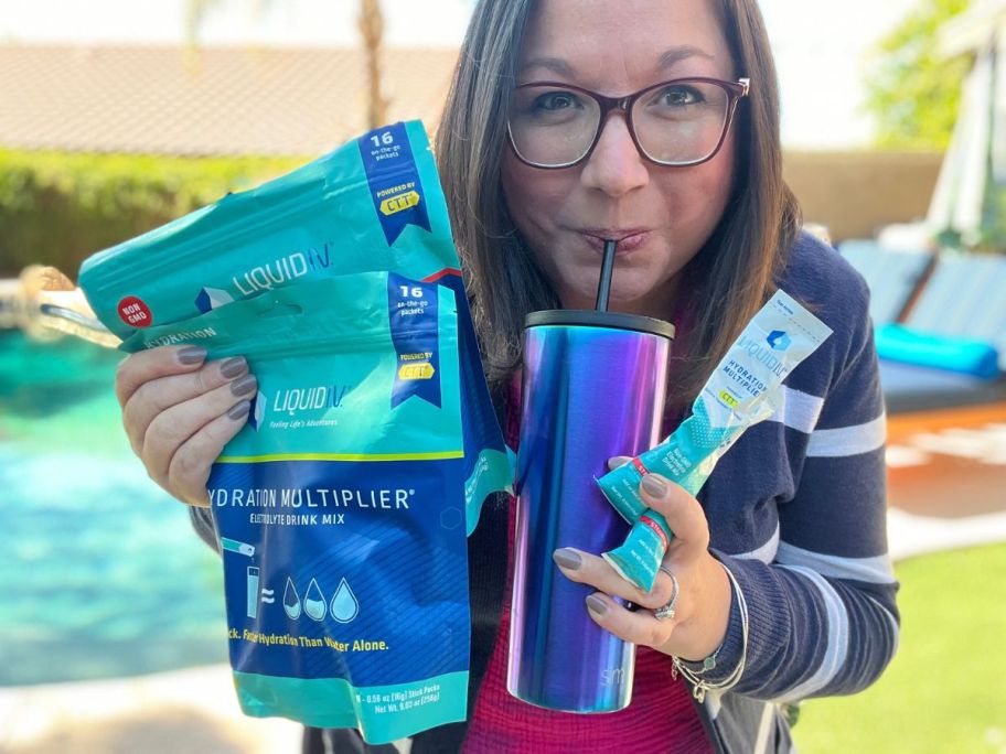 woman holding Liquid IV bag and packet while sipping out a of a tumbler