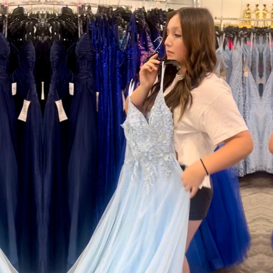 teen holding up blue dress in store