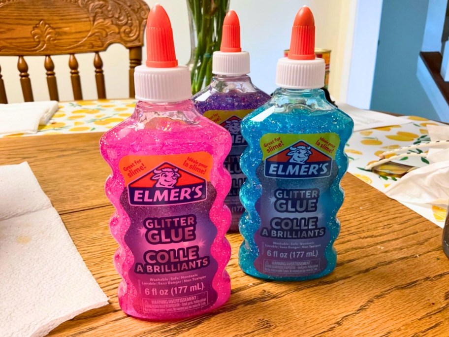 3 bottles of Elmer's Glitter Glue in pink, purple, and blue sitting on a table