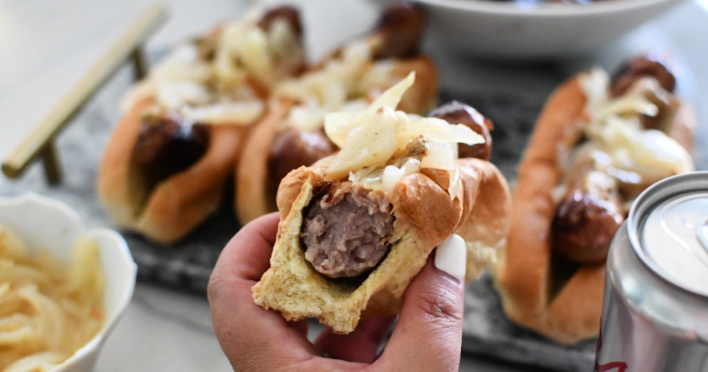 holding a beer brat with onions and mustard 