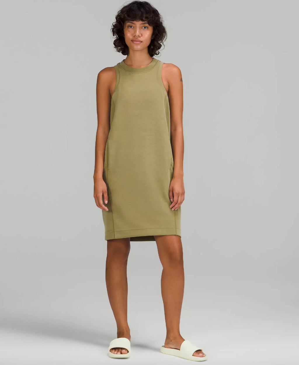 woman wearing green dress and white slides in gray room