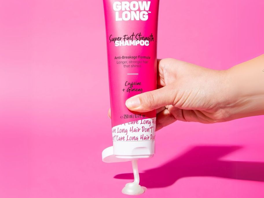hand squeezing Marc Anthony Strengthening Biotin Shampoo tube onto table