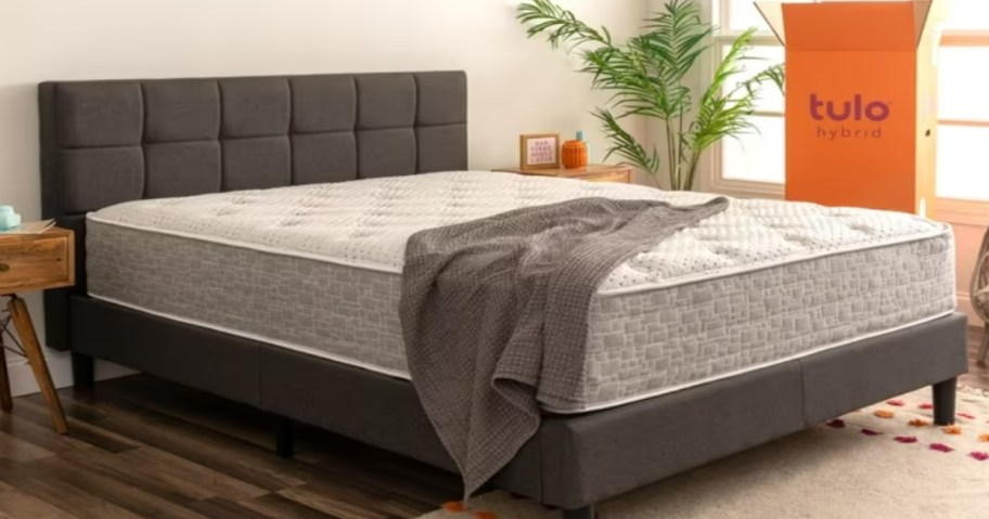 a mattress on a grey platform bed frame with an orange box next to it 
