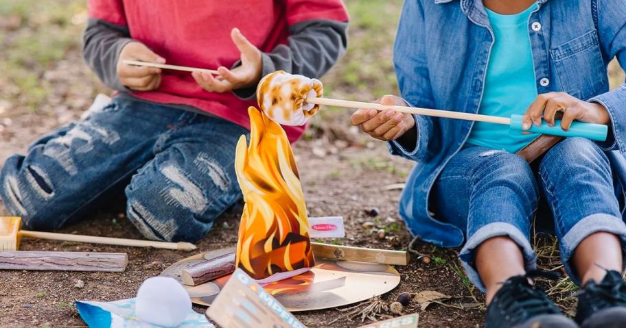 two kids pretending to roast marshmallow on Melissa & Doug Let's Explore Campfire S'Mores Play Set outside