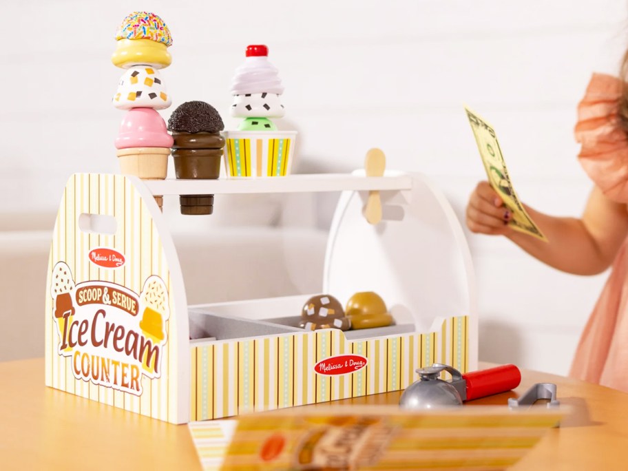 ice cream playset on table near girl holding play money