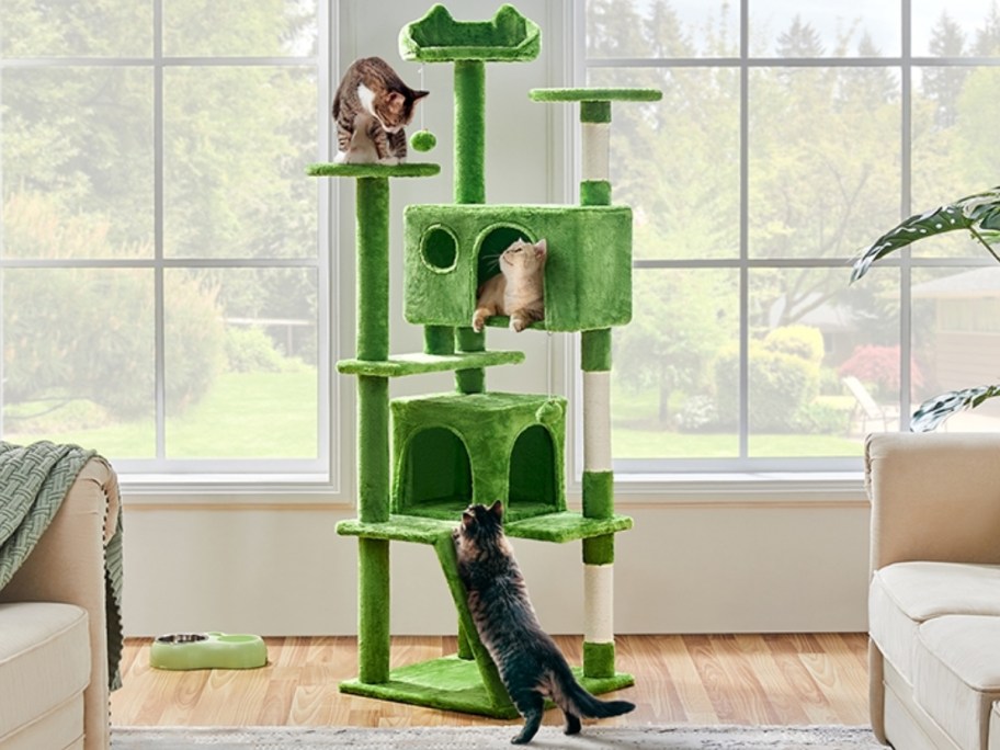 a large green tall cat tower with cats in it and climbing on it in a living room