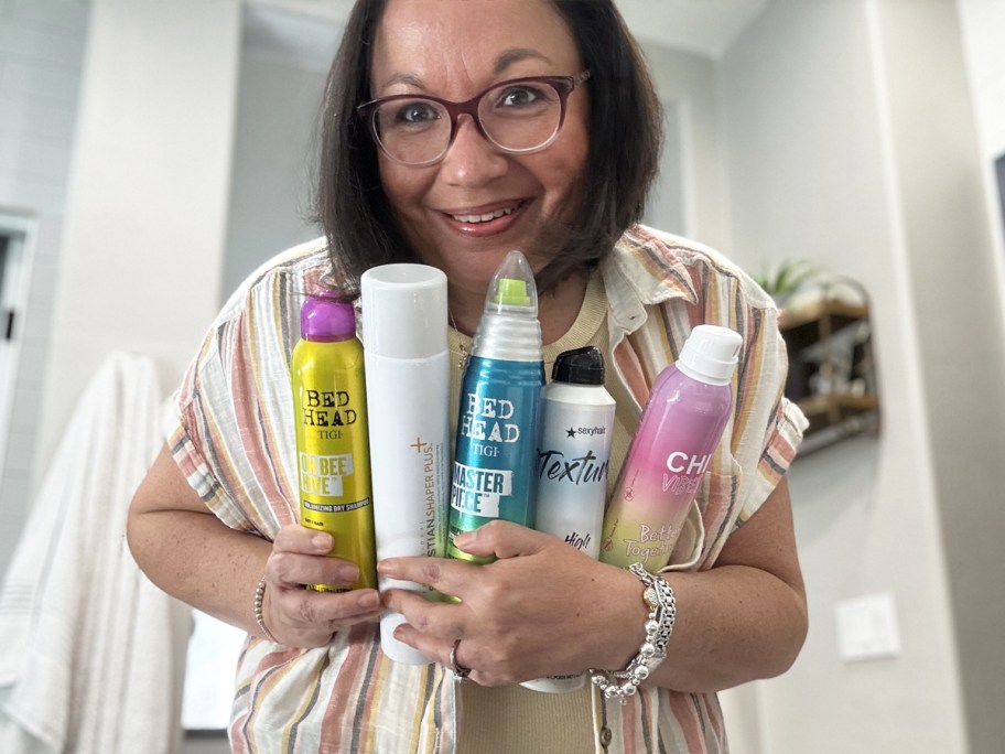 woman holding an armful of hairsprays in bathroom