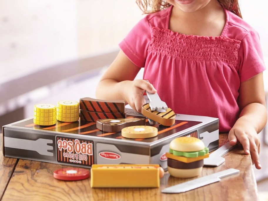 girl playing with bbq grill toy on table