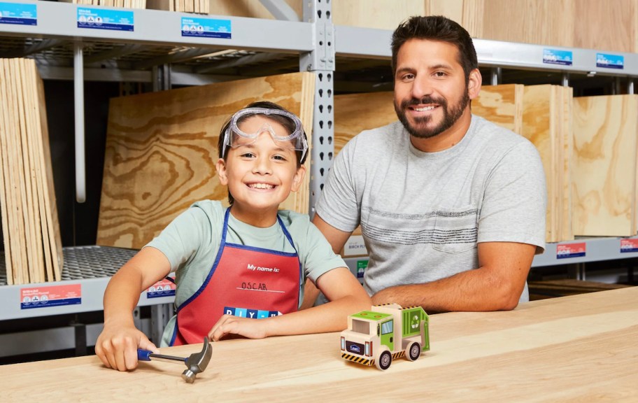 kid with dad wearing lowes apron at wood table holding hammer