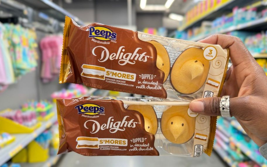 a womans hand holding two packages of s'mores flavored peeps