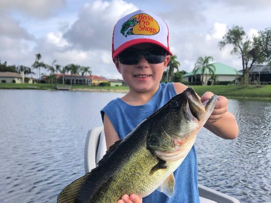 little boy in a bass pro shops hat holding a large fish