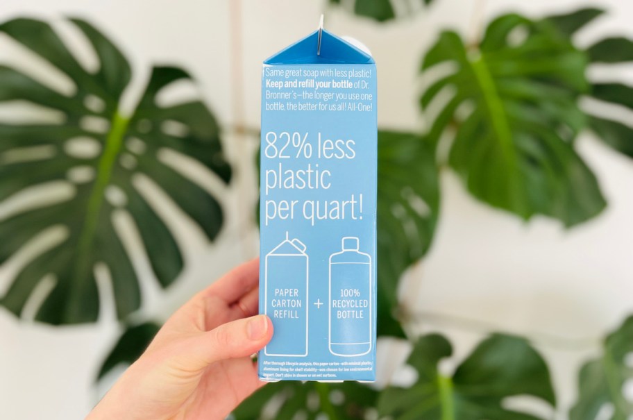 hand holding refill carton of soap in front of plant