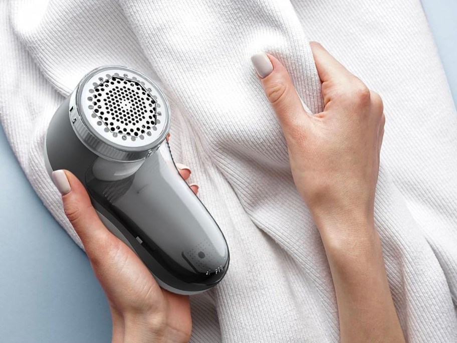 hand holding gray and white fabric shaver and white sweater