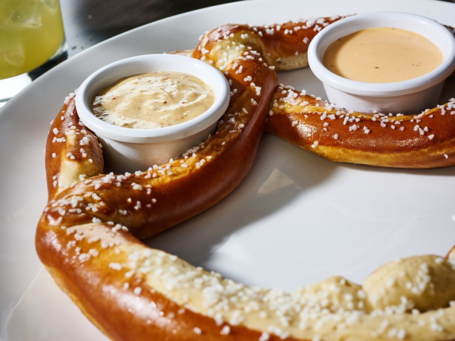 large soft pretzel on a white plate with 2 dipping sauces
