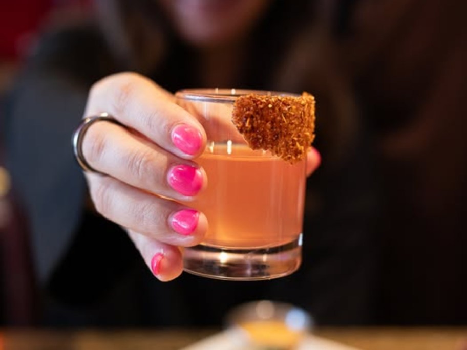 woman holding a tajin-rimmed shot glass