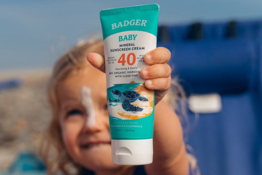 baby girl holding sunscreen tube in air
