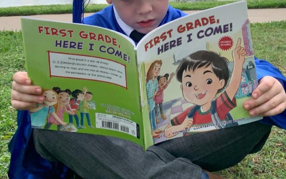 boy with grad cap holding first grade here i come book