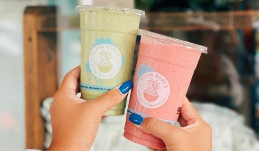 two hands holding green and pink playa bowl smoothies