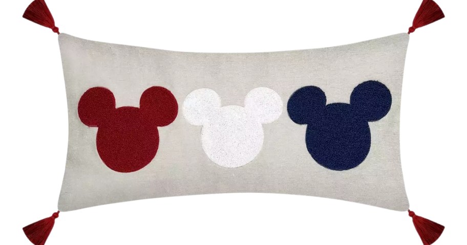 a tan color rectangle throw pillow with red, white, and blue Mickey Mouse heads and tassels