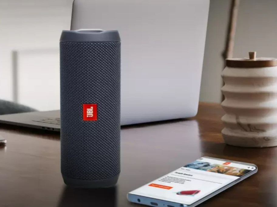 a grey JBL bluetooth speaker on a desk with a laptop and smart phone